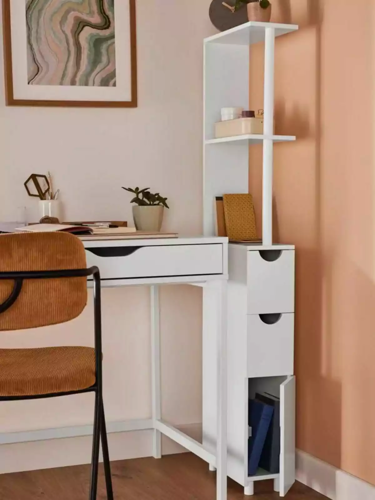 Un escritorio blanco con estanterías integradas, decorado con una planta, libros y una silla marrón, en una habitación con paredes color durazno y un cuadro abstracto. Un escritorio blanco con estanterías integradas, decorado con una planta, libros y una silla marrón, en una habitación con paredes color durazno y un cuadro abstracto.