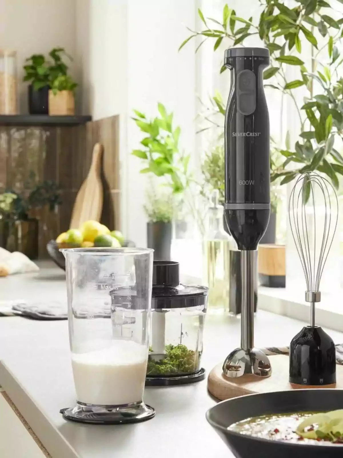 Una batidora de mano negra con accesorios y un vaso medidor en una cocina moderna iluminada por la luz natural. Una batidora de mano negra con accesorios y un vaso medidor en una cocina moderna iluminada por la luz natural.