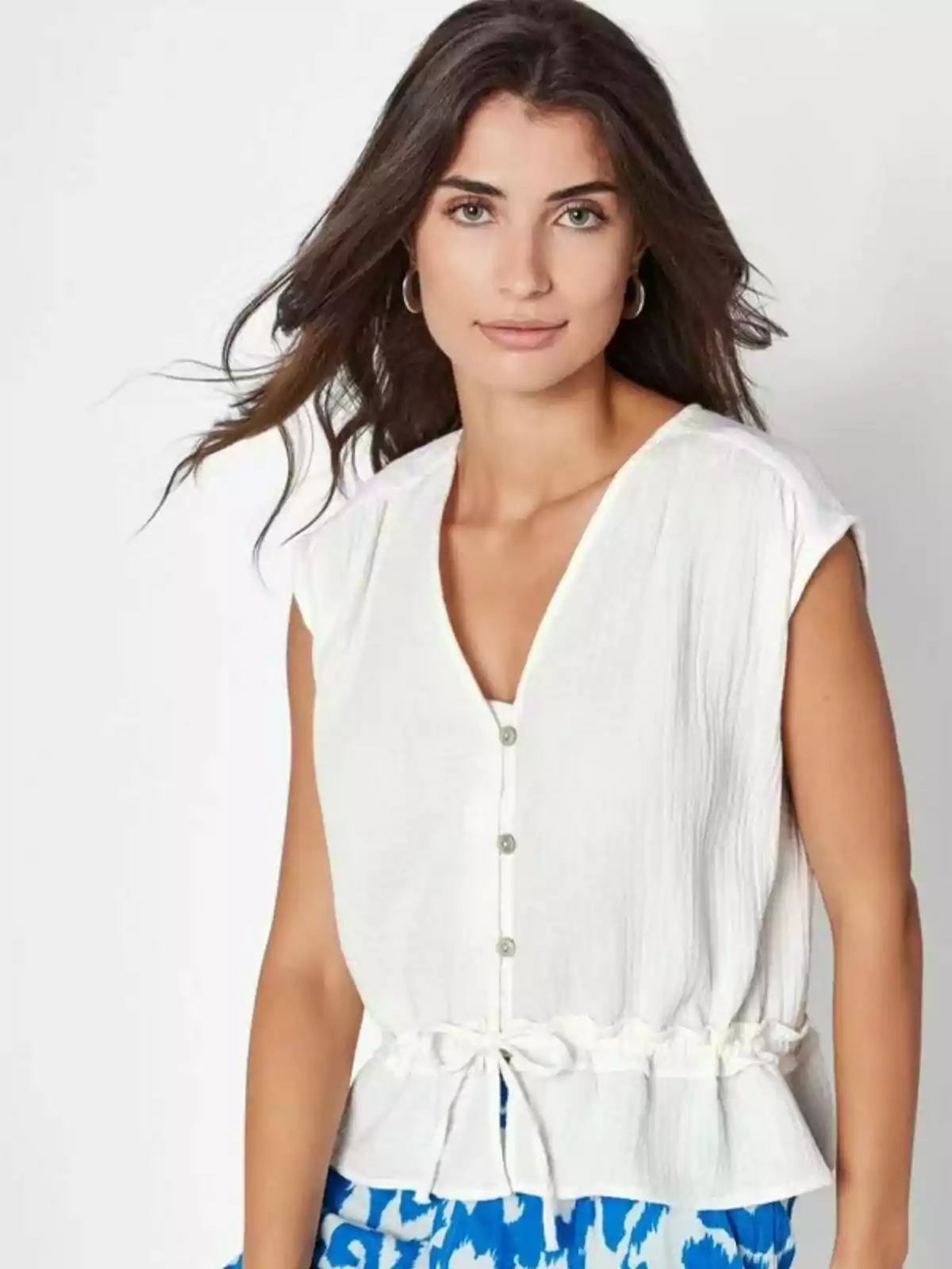 Mujer de cabello castaño largo con blusa blanca sin mangas y pantalón azul con estampado blanco mirando a la cámara Mujer de cabello castaño largo con blusa blanca sin mangas y pantalón azul con estampado blanco mirando a la cámara