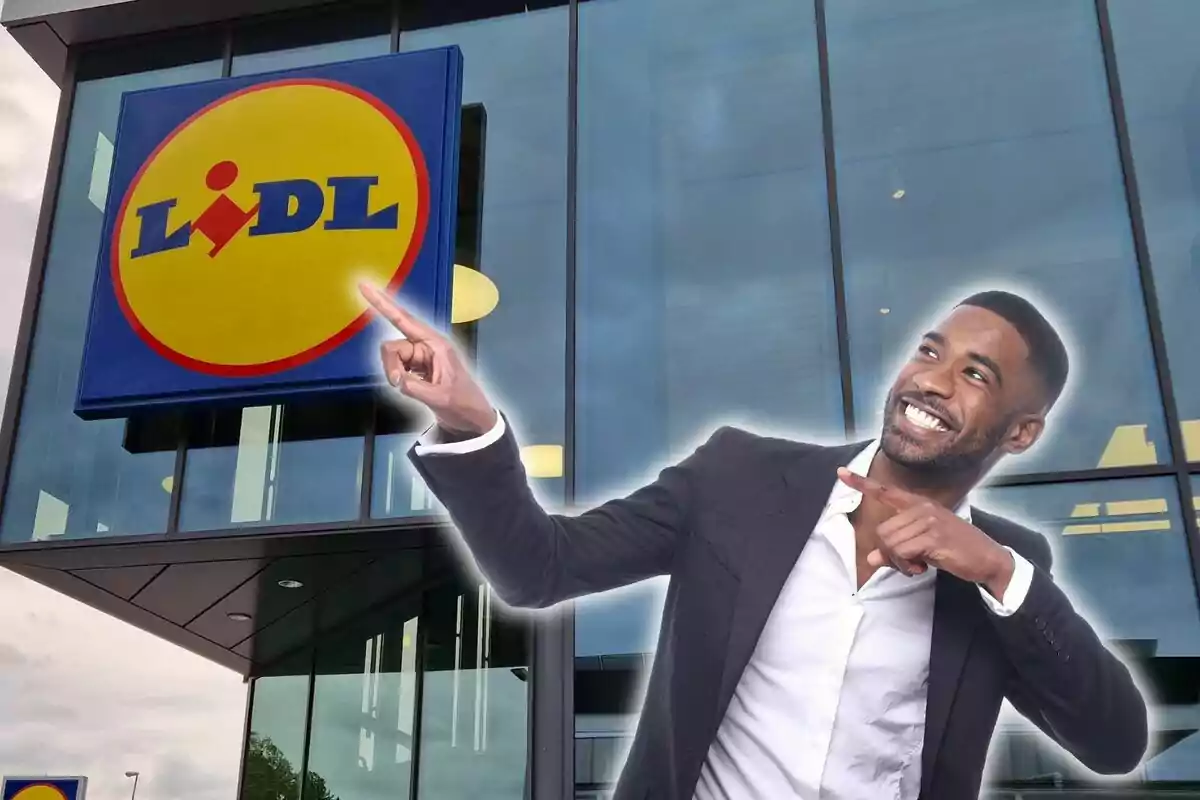 Un hombre sonriente con traje oscuro y camisa blanca señala con entusiasmo el logotipo de Lidl en la fachada de una tienda.