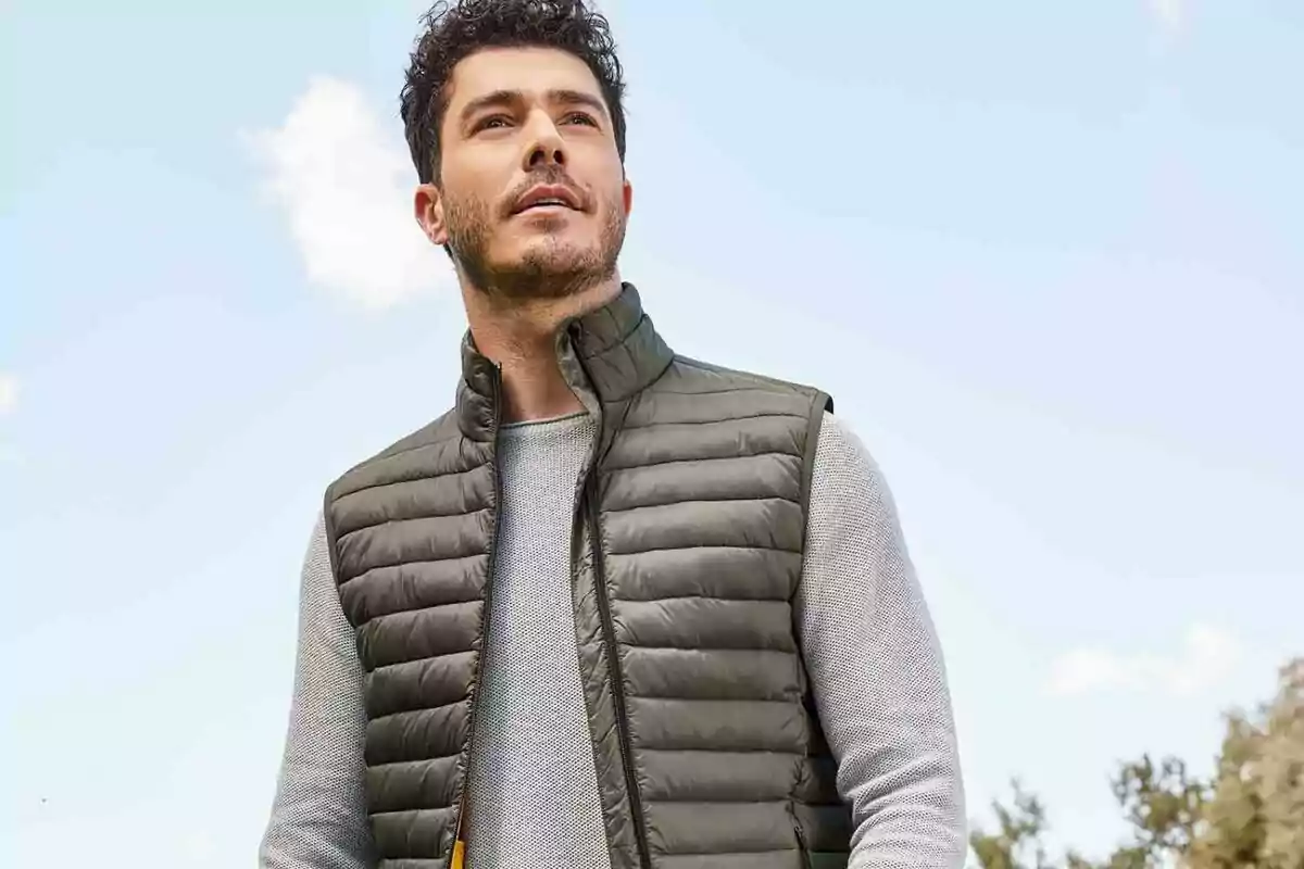 Hombre con chaleco acolchado verde y suéter gris mirando hacia arriba con un cielo azul de fondo. Hombre con chaleco acolchado verde y suéter gris mirando hacia arriba con un cielo azul de fondo.