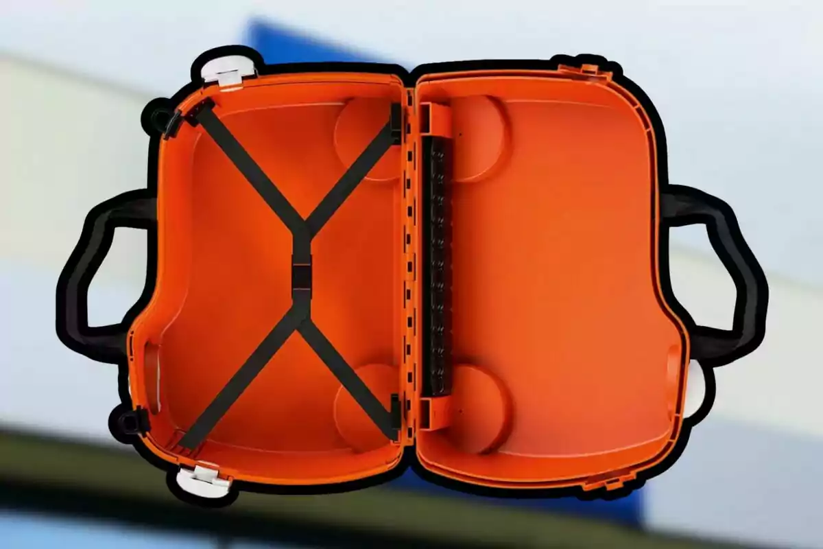 Una maleta de color naranja abierta mostrando su interior con correas negras y un fondo desenfocado. Una maleta de color naranja abierta mostrando su interior con correas negras y un fondo desenfocado.