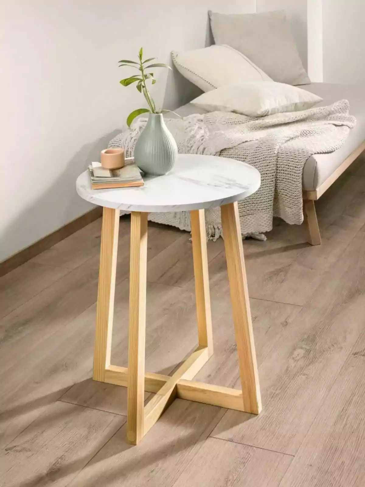 Mesa auxiliar de madera con tapa de mármol, decorada con un jarrón verde con planta, una vela y libros, junto a un sofá con cojines y manta en una habitación de estilo minimalista. Mesa auxiliar de madera con tapa de mármol, decorada con un jarrón verde con planta, una vela y libros, junto a un sofá con cojines y manta en una habitación de estilo minimalista.