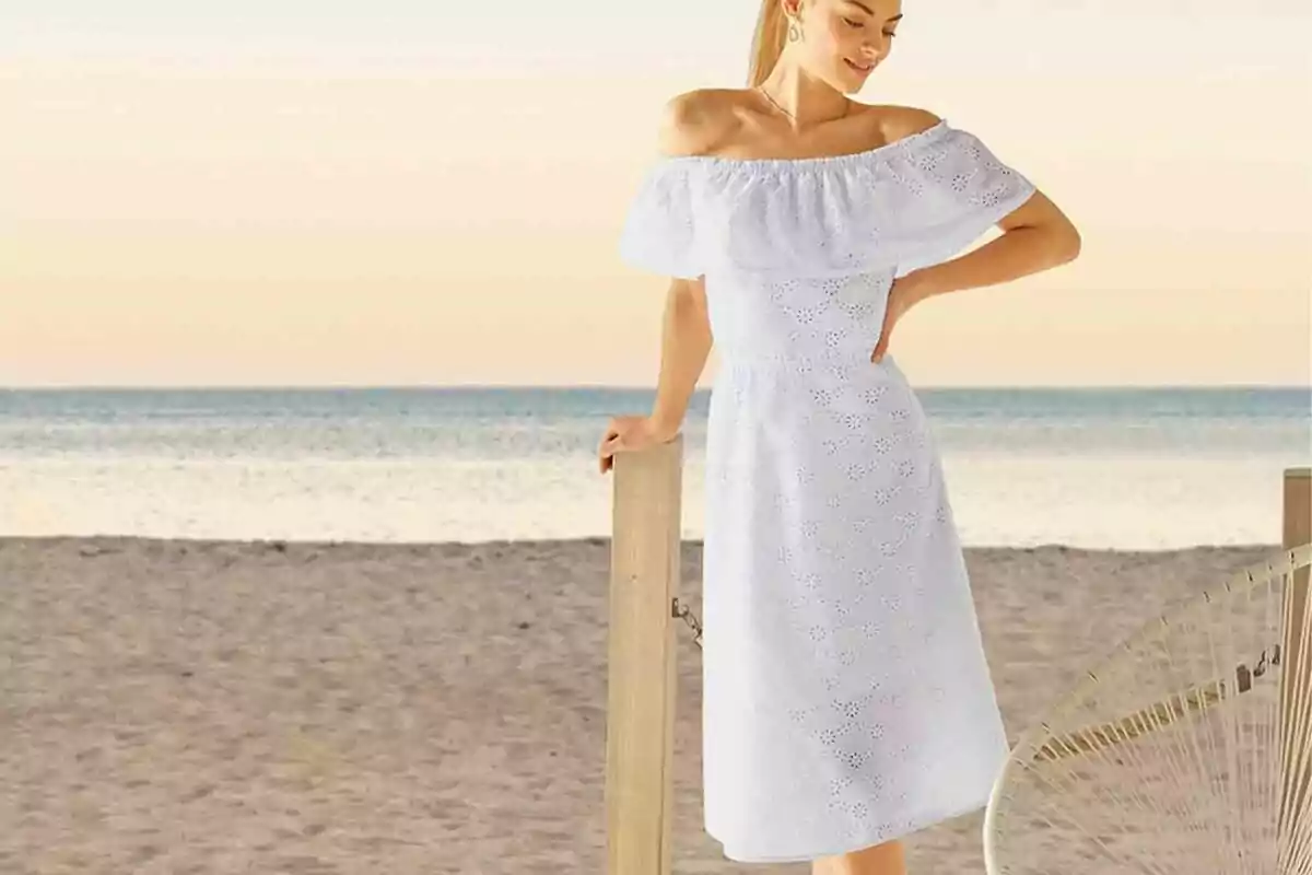 Mujer con vestido blanco de hombros descubiertos posando en la playa al atardecer Mujer con vestido blanco de hombros descubiertos posando en la playa al atardecer