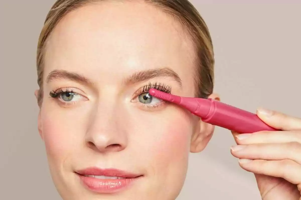 Mujer usando un rizador de pestañas eléctrico rosa en su ojo derecho Mujer usando un rizador de pestañas eléctrico rosa en su ojo derecho