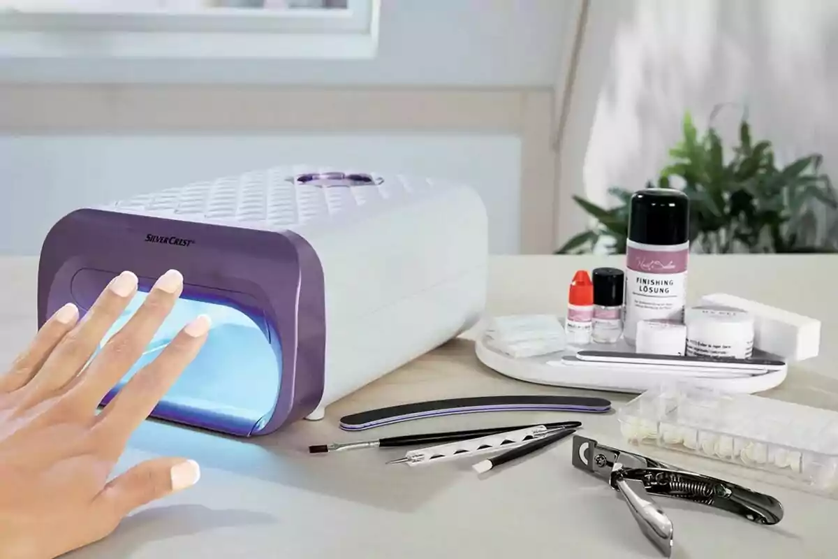 Una mano bajo una lámpara de uñas UV con herramientas y productos de manicura sobre una mesa. Una mano bajo una lámpara de uñas UV con herramientas y productos de manicura sobre una mesa.