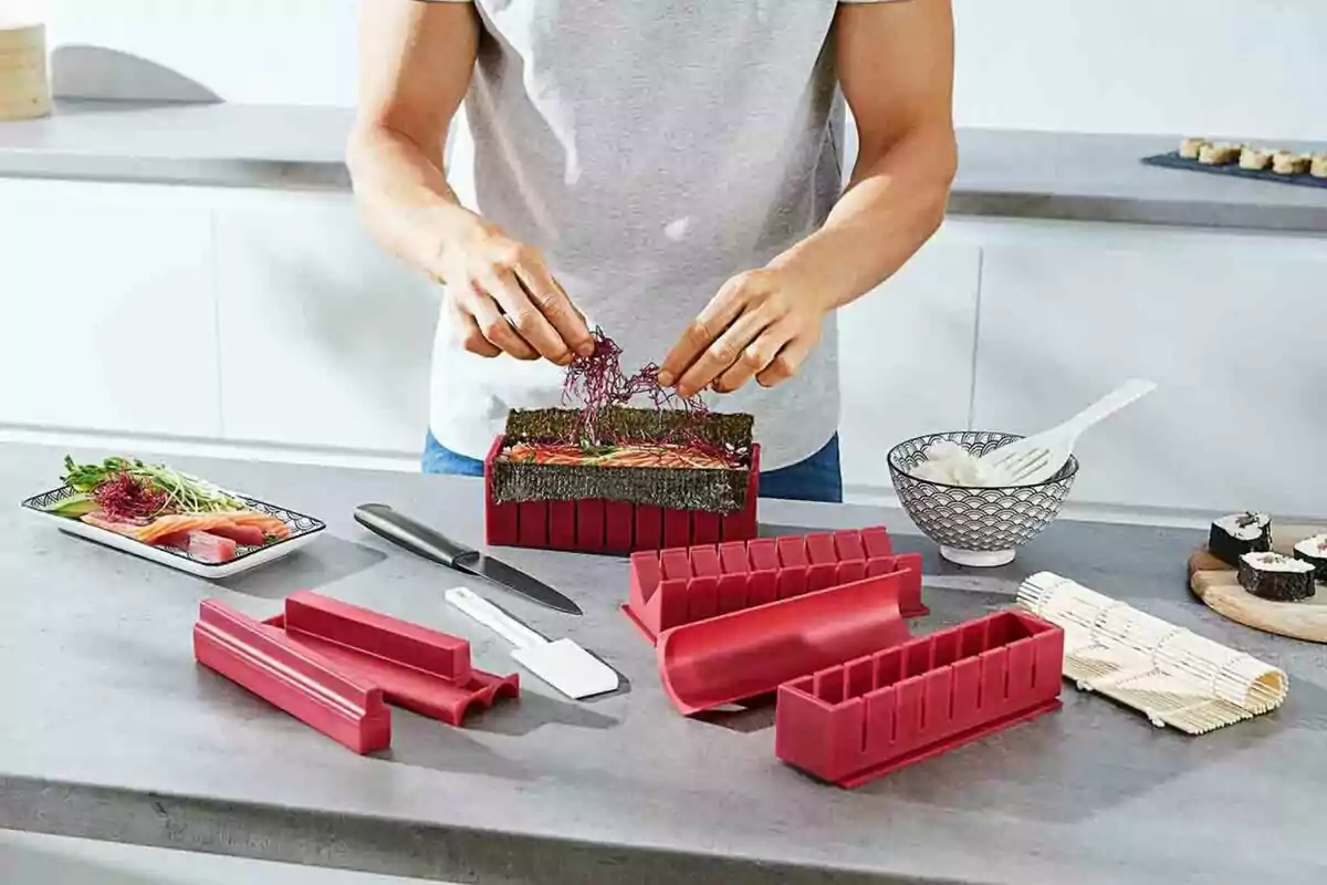 Persona preparando sushi en una cocina con moldes y utensilios específicos para hacer sushi. Persona preparando sushi en una cocina con moldes y utensilios específicos para hacer sushi.
