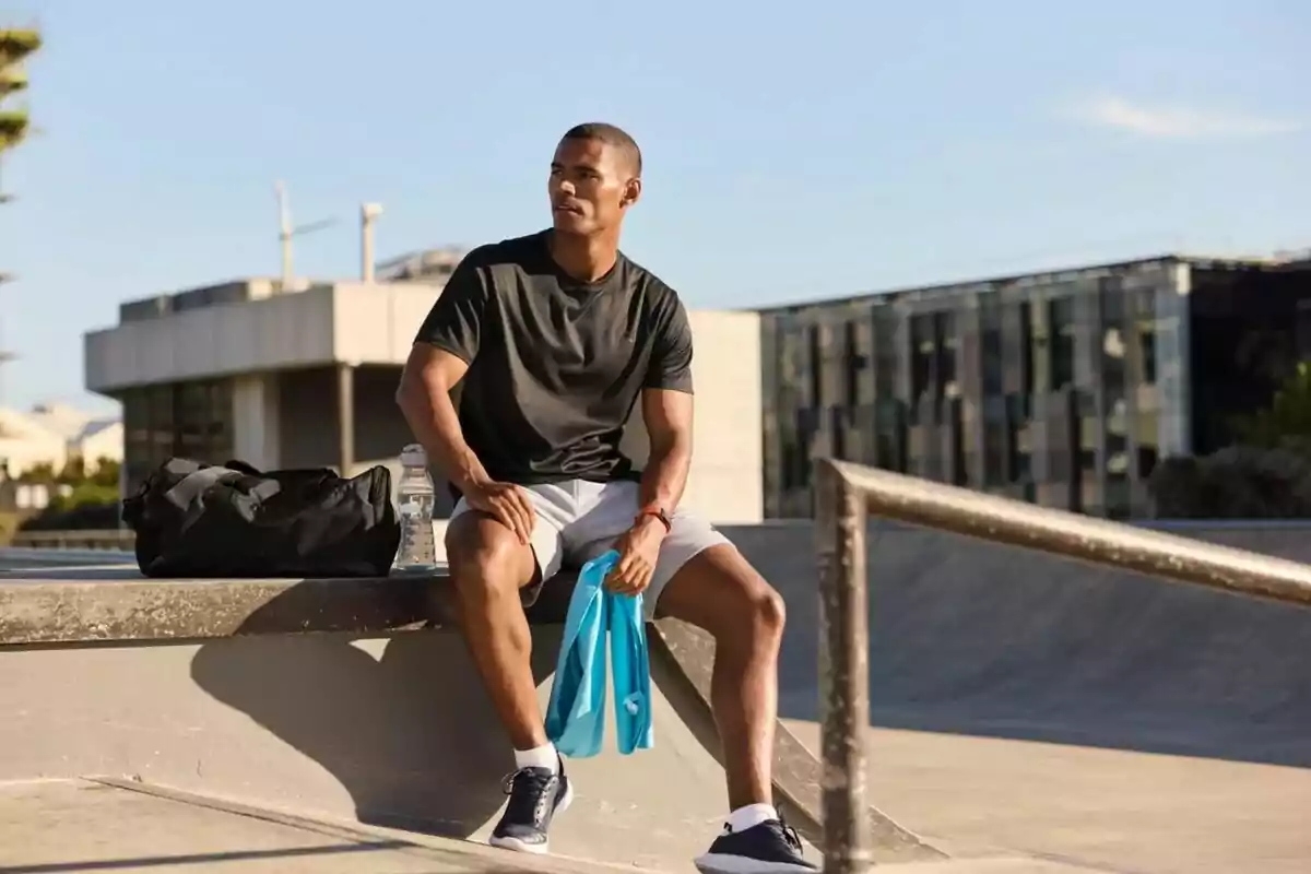 Un hombre sentado en un parque de skate con ropa deportiva, una bolsa de gimnasio y una botella de agua. Un hombre sentado en un parque de skate con ropa deportiva, una bolsa de gimnasio y una botella de agua.