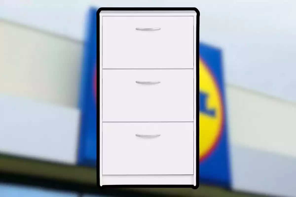 Un mueble de almacenamiento blanco con tres cajones frente a un fondo borroso que parece ser el logotipo de una tienda. Un mueble de almacenamiento blanco con tres cajones frente a un fondo borroso que parece ser el logotipo de una tienda.