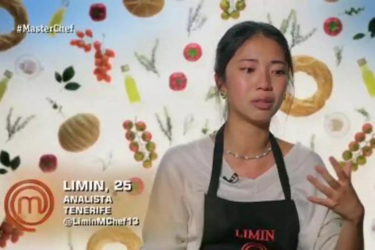 Limin con delantal negro aparece en un programa de cocina, con un fondo decorado con imágenes de ingredientes como tomates, panes y botellas de aceite en MasterChef. Limin con delantal negro aparece en un programa de cocina, con un fondo decorado con imágenes de ingredientes como tomates, panes y botellas de aceite en MasterChef.