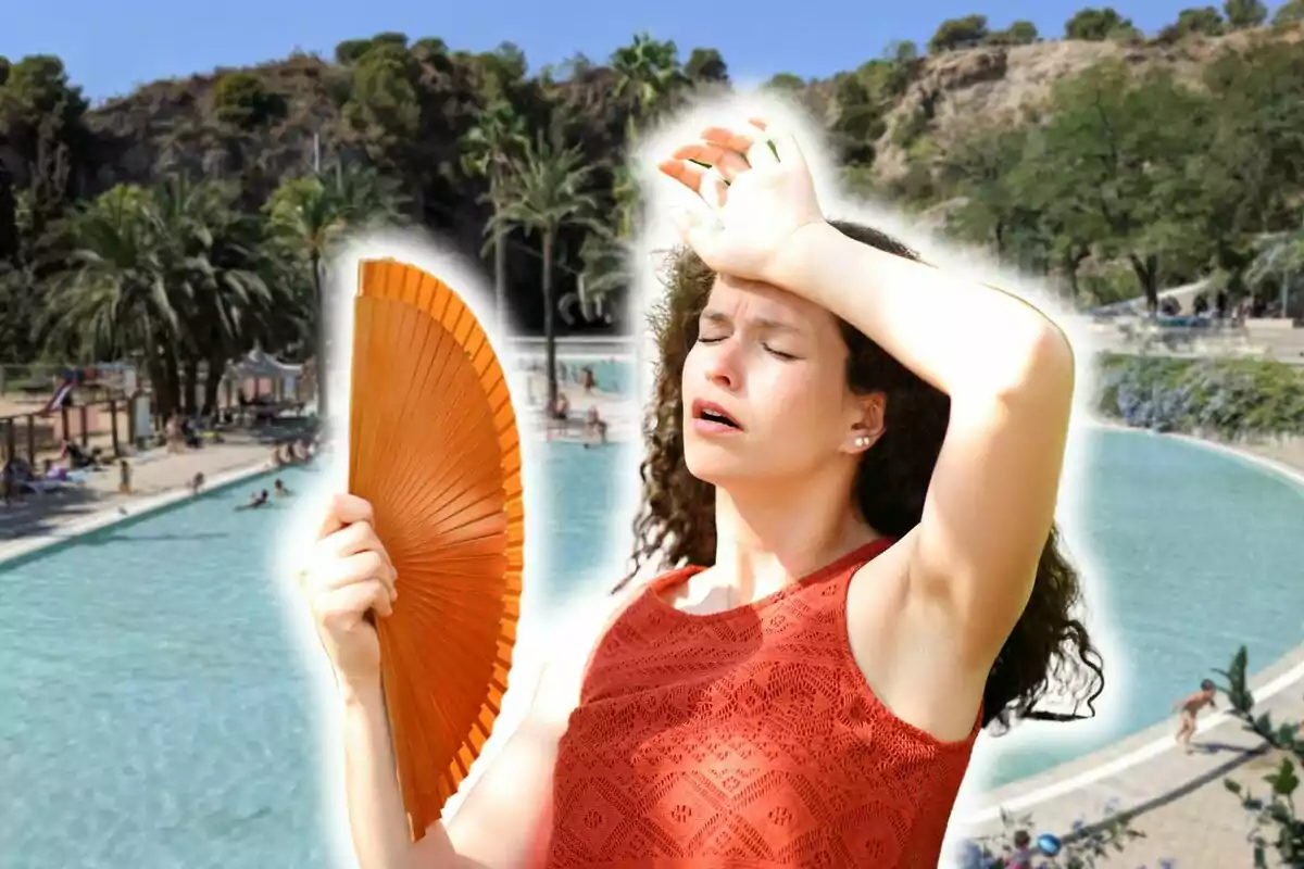 Una mujer con un vestido naranja se abanica mientras se protege del sol con la mano en la frente, en el fondo hay una piscina con personas disfrutando del agua y palmeras alrededor.