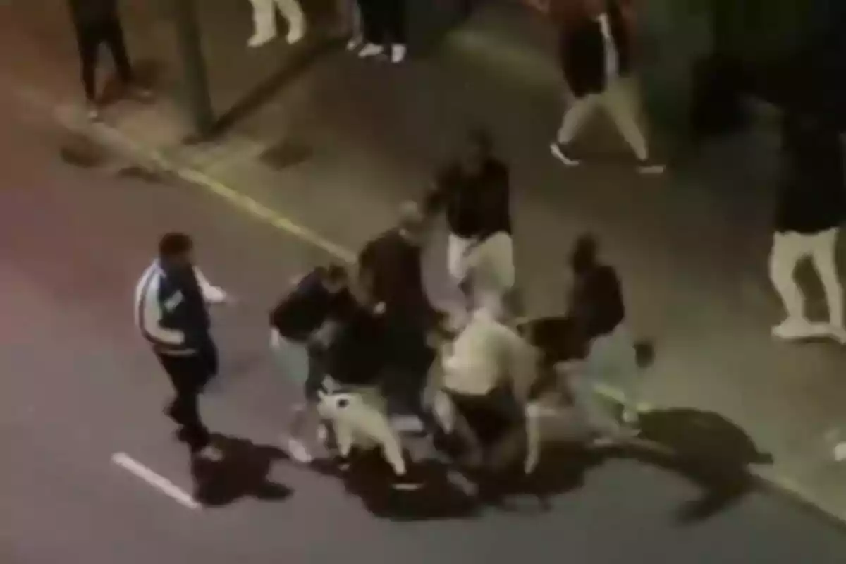 Un grupo de personas en una calle durante la noche, algunas parecen estar involucradas en un altercado físico.