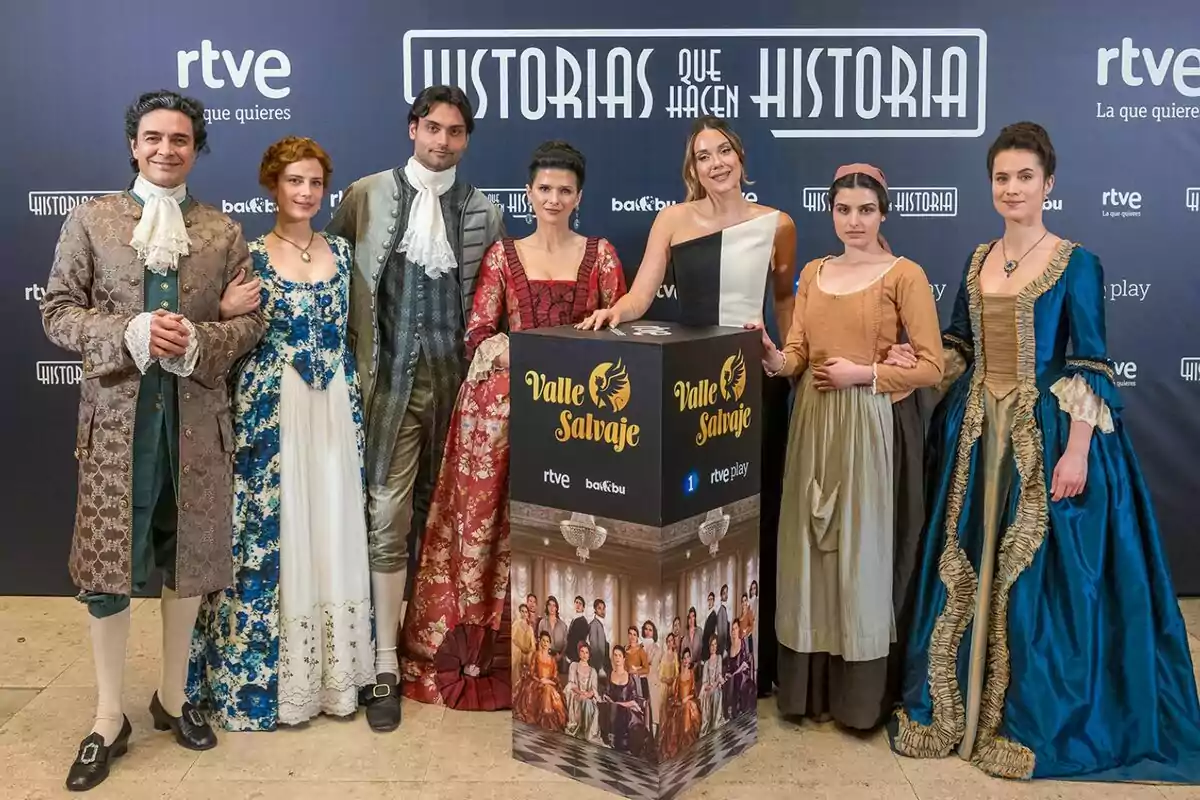 Un grupo de personas vestidas formado por José Manuel Seda, Rocio Suárez de Puga, Sabela Arán, Marco Pernas, Loren Mairena y Miren Arrieta con trajes de época junto a Lorena Gómez posan frente a un fondo promocional de Un grupo de personas vestidas formado por José Manuel Seda, Rocio Suárez de Puga, Sabela Arán, Marco Pernas, Loren Mairena y Miren Arrieta con trajes de época junto a Lorena Gómez posan frente a un fondo promocional de