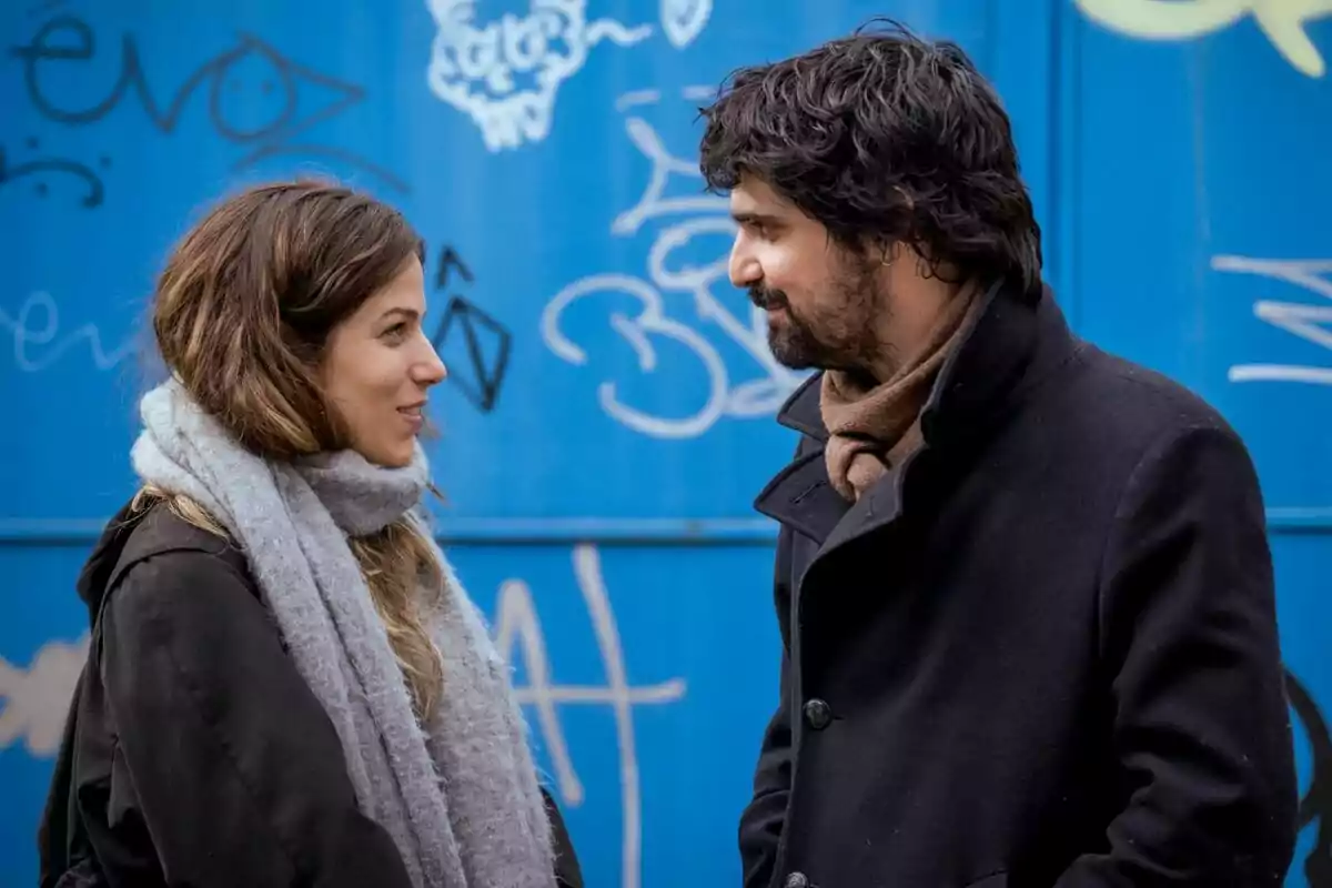 Iria del Río y Francesco Carril conversando frente a una pared azul con grafitis en la serie Los Años Nuevos.