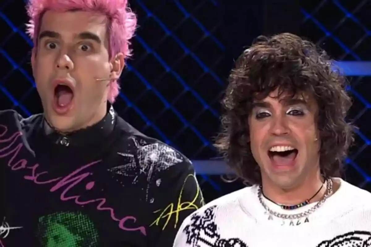 Javi Calvo y Javi Ambrossi con expresiones de sorpresa y alegría, una con cabello rosado y otra con cabello rizado, en un escenario iluminado en Mask Singer.