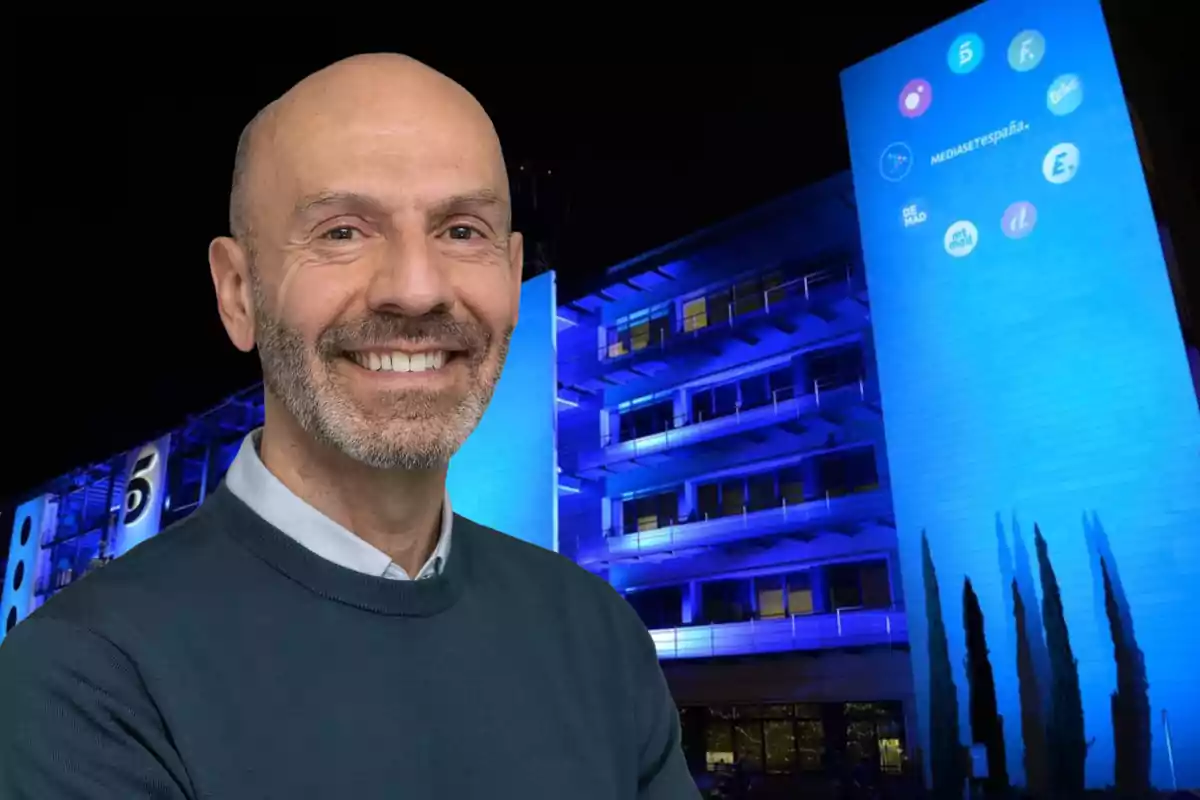 Alberto Carullo sonriente con barba y suéter oscuro frente al edificio de Mediaset España iluminado de azul por la noche.