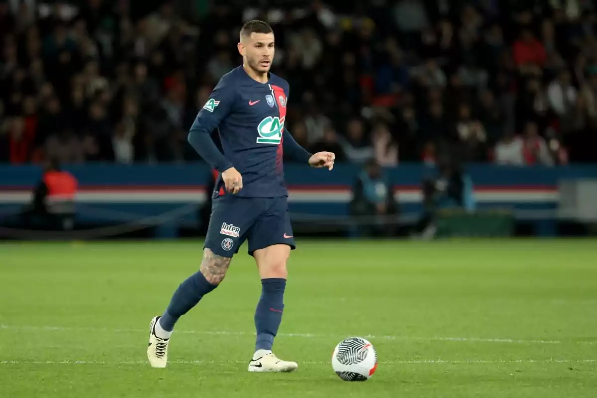 Un jugador de fútbol con uniforme azul oscuro controla el balón en un campo de juego durante un partido. Un jugador de fútbol con uniforme azul oscuro controla el balón en un campo de juego durante un partido.