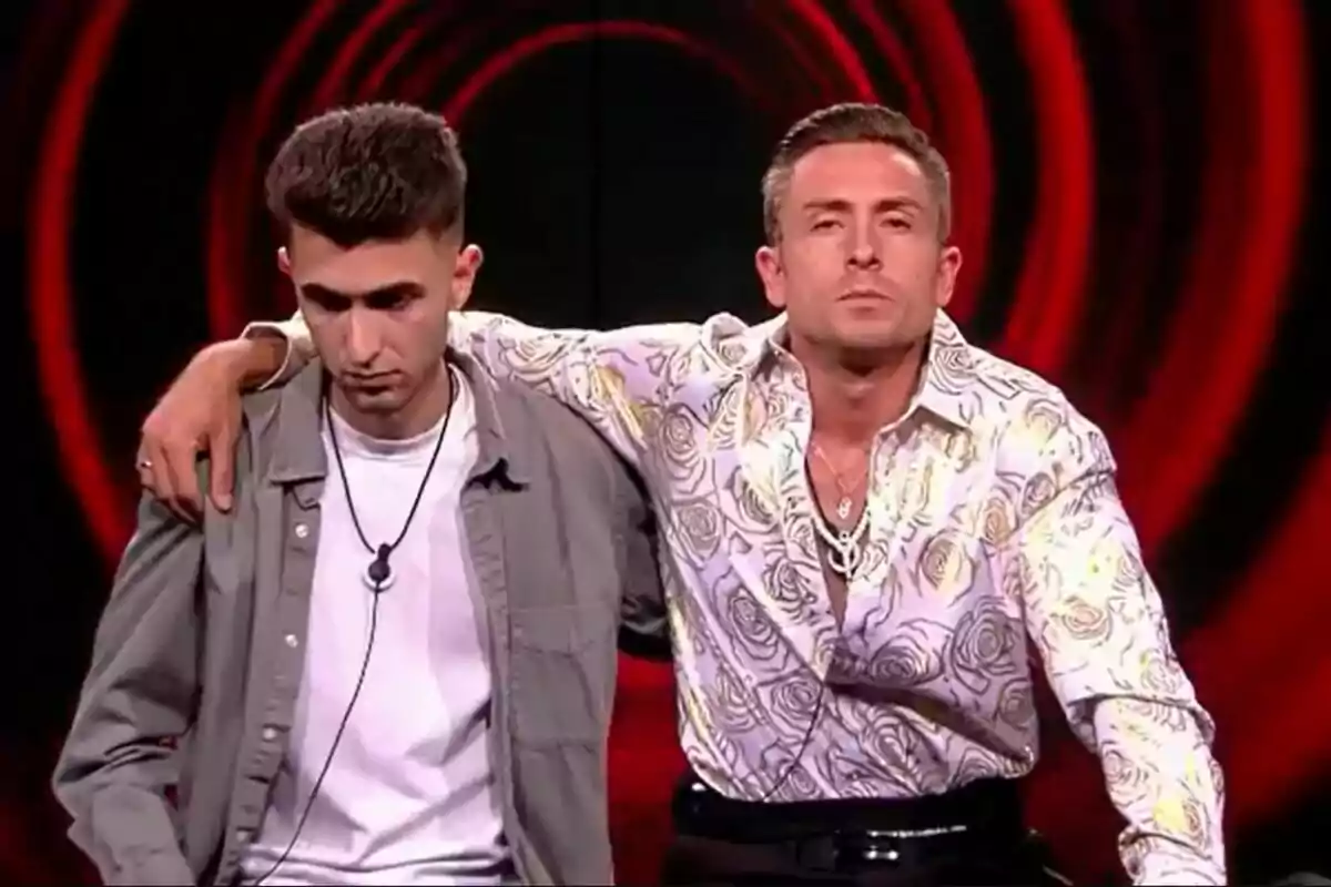 Juan y Luis posan juntos, uno con una camisa gris y el otro con una camisa blanca con estampado floral, sobre un fondo con círculos rojos en Gran Hermano.