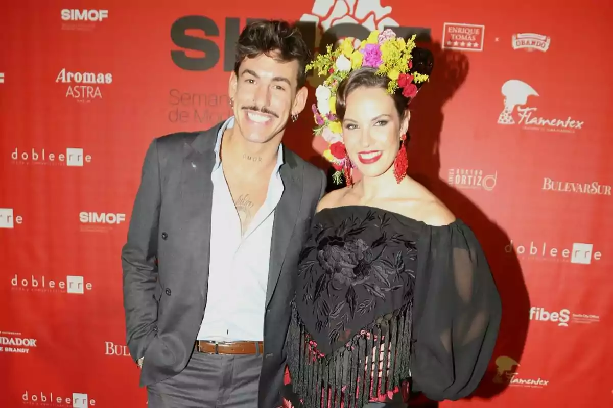 Luitingo sonriendo en traje gris junto a Jessica Bueno sonriendo con flores en el pelo, los labios rojos y un mantón negro Luitingo sonriendo en traje gris junto a Jessica Bueno sonriendo con flores en el pelo, los labios rojos y un mantón negro