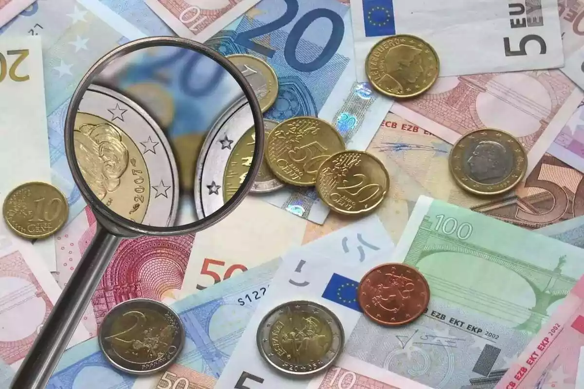 Montaje de unos billetes y una lupa con unas monedas de 2 euros