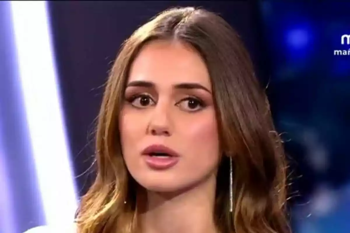 Maica Benedito con cabello castaño y aretes largos en un entorno de estudio iluminado en Gran Hermano.