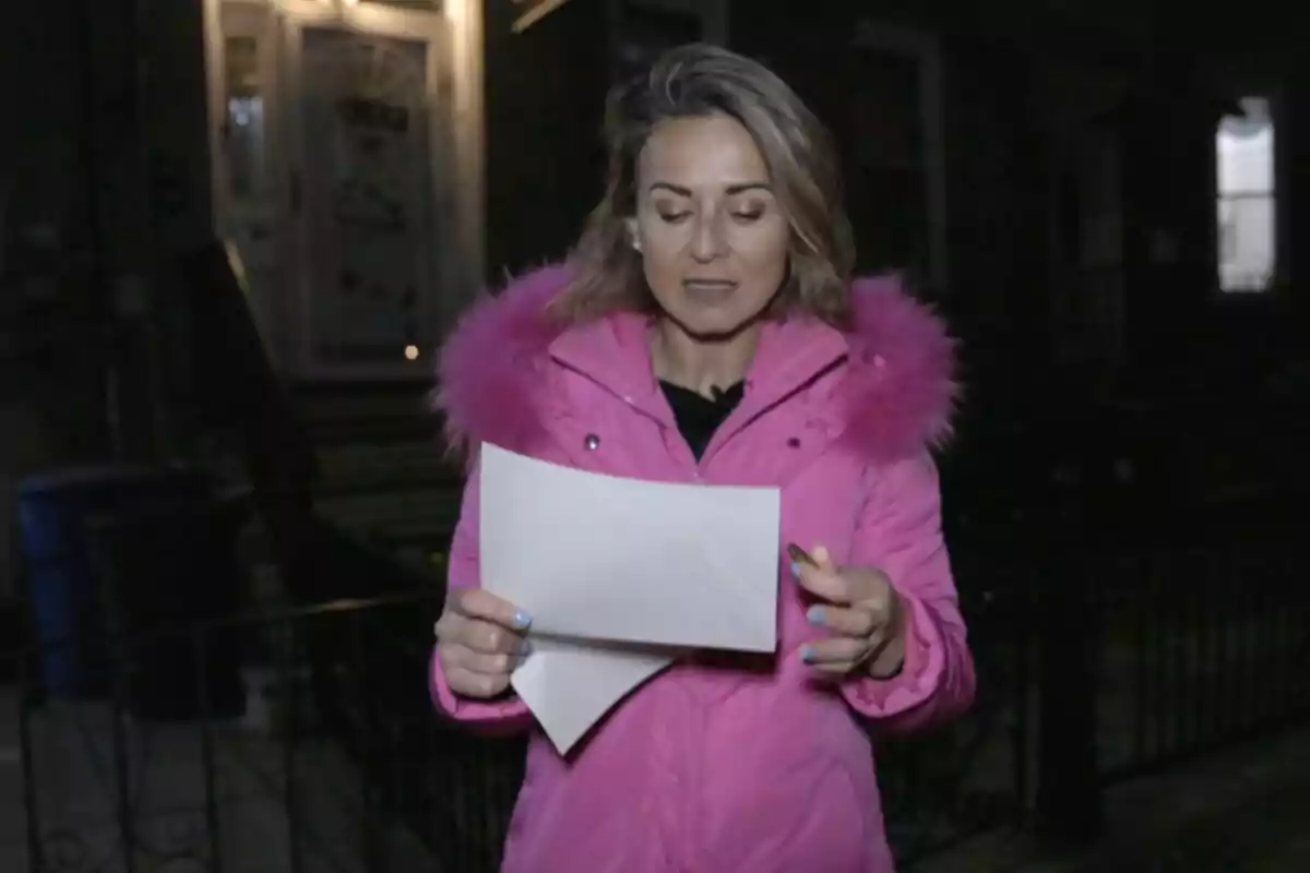 Mamen Salas con abrigo rosa sostiene una hoja de papel mientras está de pie frente a una casa de noche en 'Cuarto Milenio'. Mamen Salas con abrigo rosa sostiene una hoja de papel mientras está de pie frente a una casa de noche en 'Cuarto Milenio'.
