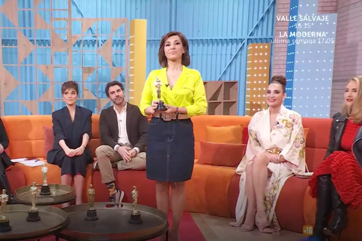 Un grupo de personas está sentado en un set de televisión colorido, con una mujer de pie sosteniendo un trofeo. Captura de 'Mañaneros' Un grupo de personas está sentado en un set de televisión colorido, con una mujer de pie sosteniendo un trofeo. Captura de 'Mañaneros'