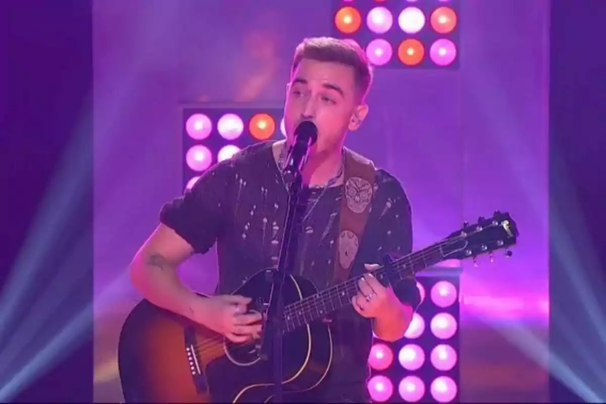 Manel Navarro tocando la guitarra y cantando en un escenario iluminado con luces de colores en un plató de TV3. Manel Navarro tocando la guitarra y cantando en un escenario iluminado con luces de colores en un plató de TV3.