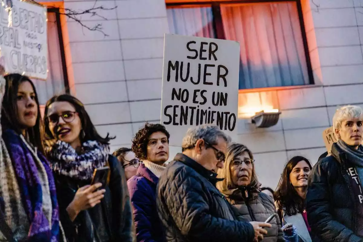 Plano medio de varios manifestantes en una protesta contra la ley Trans, con una de ellas llevando una pancarta en la que se lee la frase 'ser mujer no es un sentimiento'