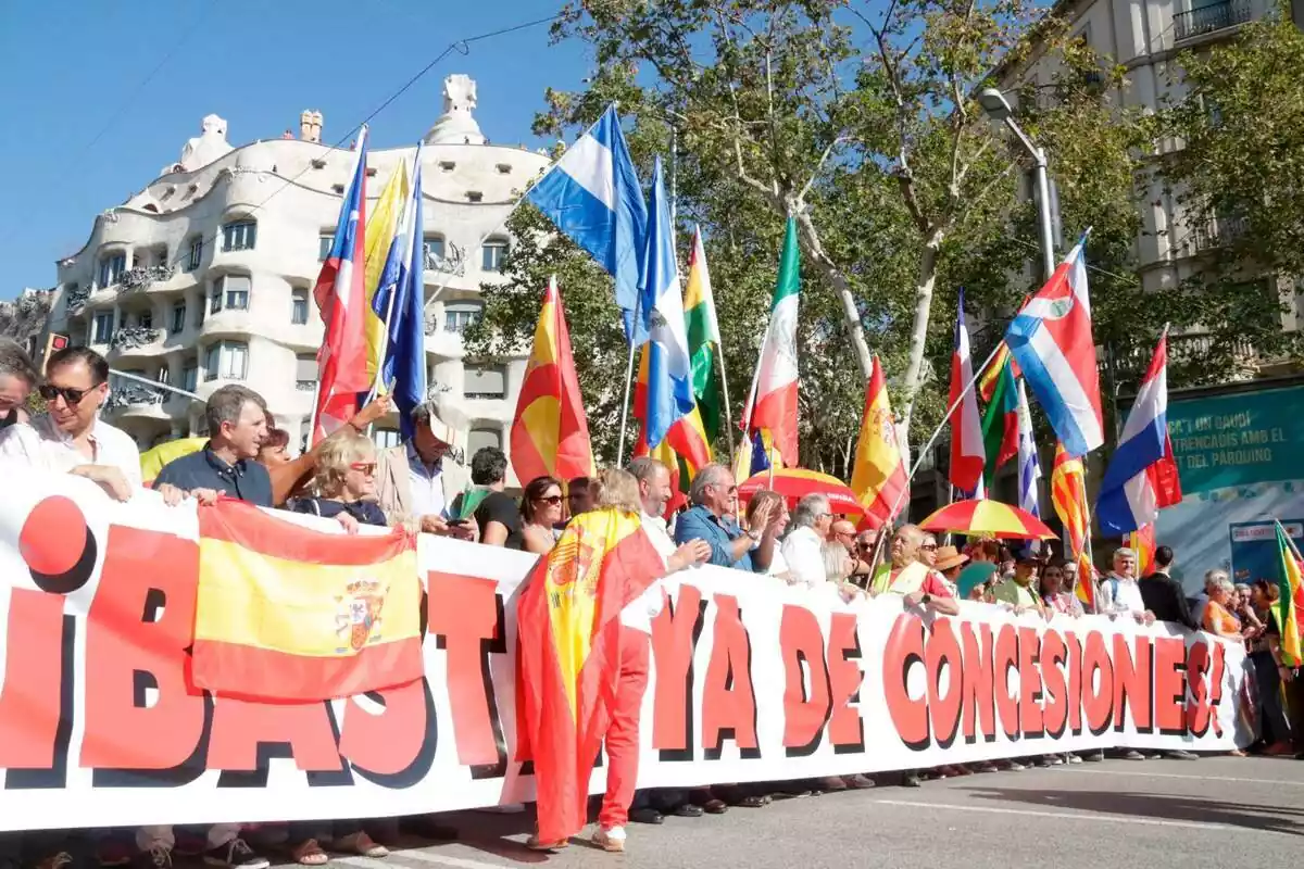 Inicio de la manifestación del 12 de octubre en Barcelona con varias personas sujetando una pancarta con el lema "basta ya de concesiones" y ondeando varias banderas de España, Honduras, Paraguay, Chile y México