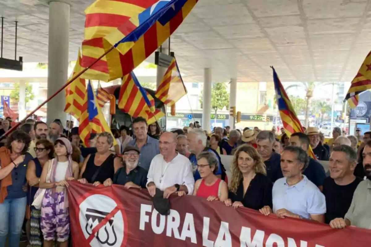 La ANC sostiene una pancarta que dice "FORA LA MONARQUIA" mientras ondean banderas con franjas rojas y amarillas en una manifestación.