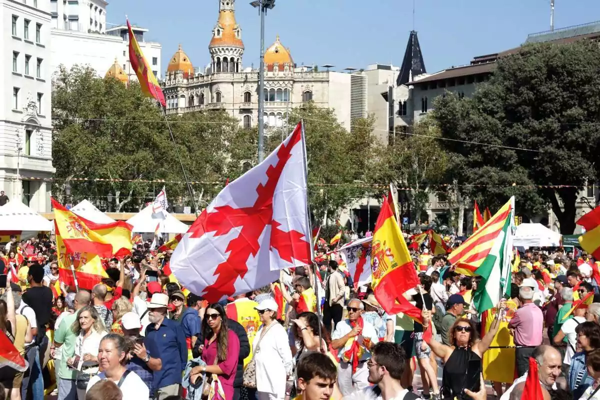 Decenas de personas en la plaza Cataluña de Barcelona celebrando el 12 de octubre con banderas españolas, carlinas y andaluzas Decenas de personas en la plaza Cataluña de Barcelona celebrando el 12 de octubre con banderas españolas, carlinas y andaluzas