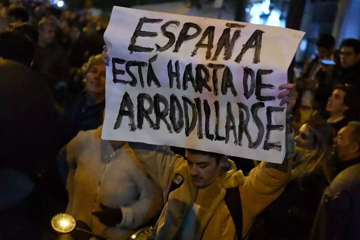 Manifestante en Ferraz mostrando una pancarta con el lema España está harta de arrodillarse