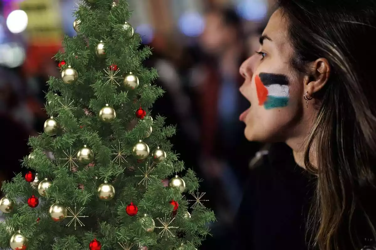 Montaje con una manifestante pro Palestina con un arbol de navidad al lado