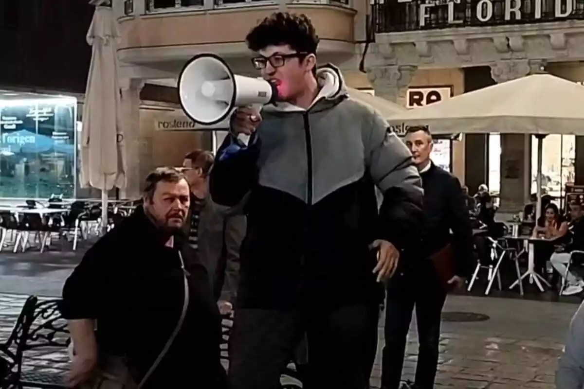 Un joven, subido a un banco, da un discurso contra los impuestos con un megáfono