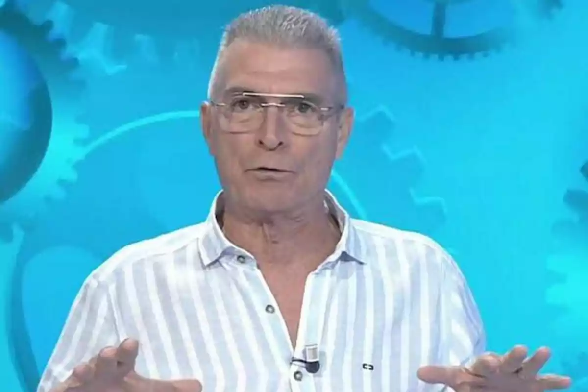 Manolo Sarria con camisa de rayas y gafas habla frente a un fondo azul con engranajes en Atrápame si puedes.