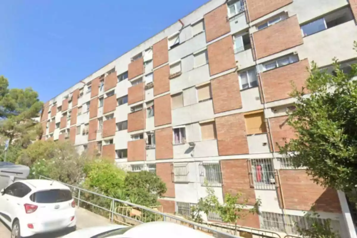 Edificio residencial de varios pisos con fachada de ladrillo y cemento, rodeado de árboles y coches estacionados en la calle Edificio residencial de varios pisos con fachada de ladrillo y cemento, rodeado de árboles y coches estacionados en la calle