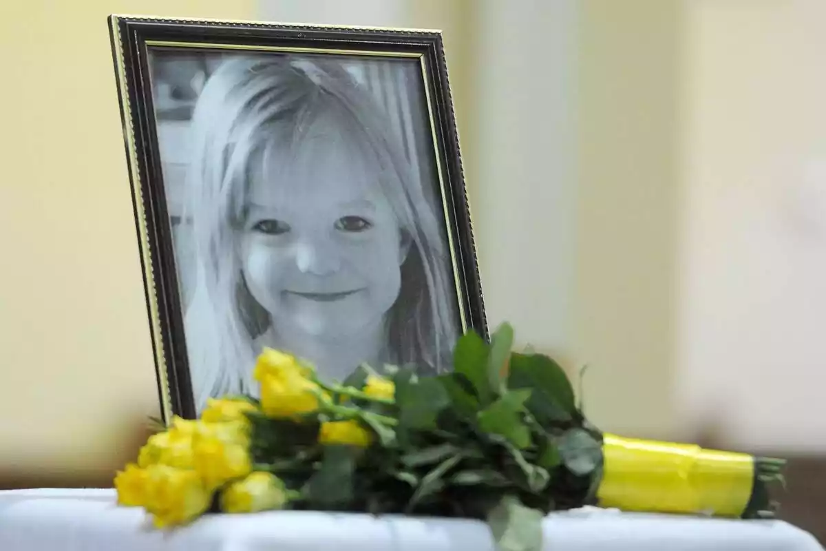 Un marco de fotos con una imagen de Madeleine McCann con unas flores amarillas delante