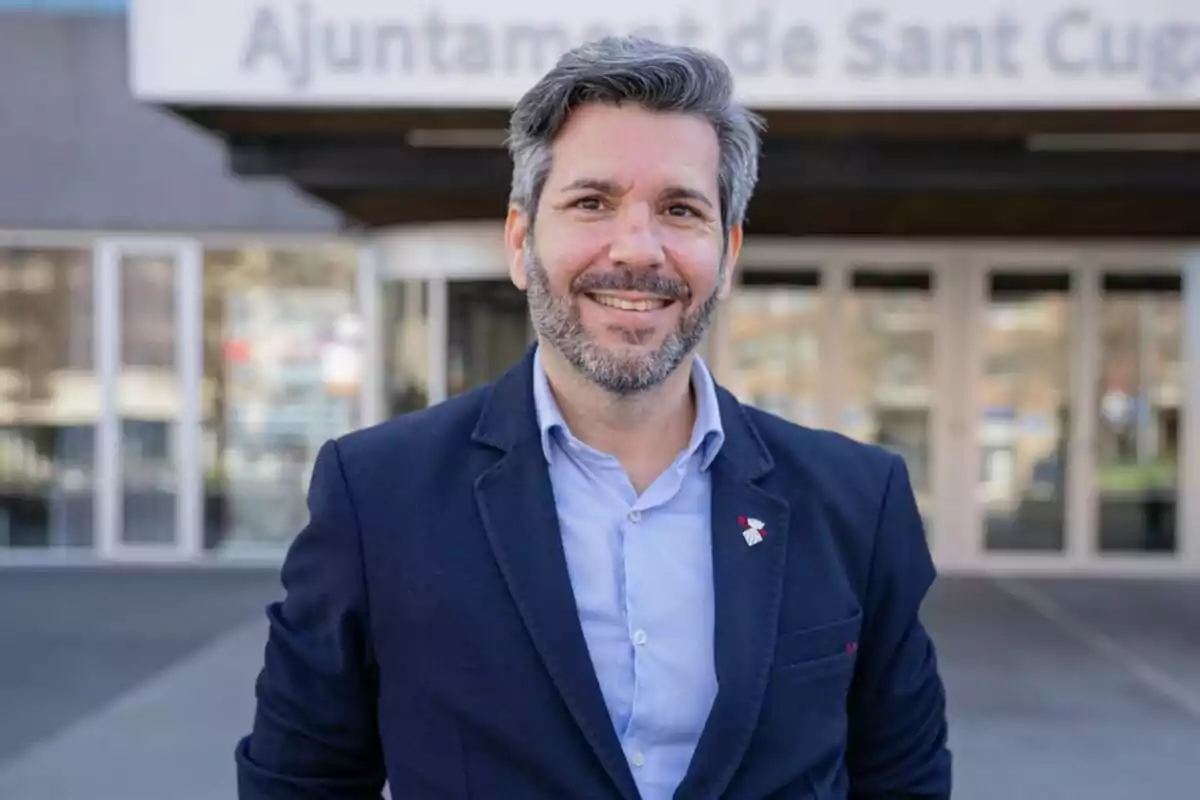 Hombre sonriendo frente a un edificio con el letrero "Ajuntament de Sant Cugat".