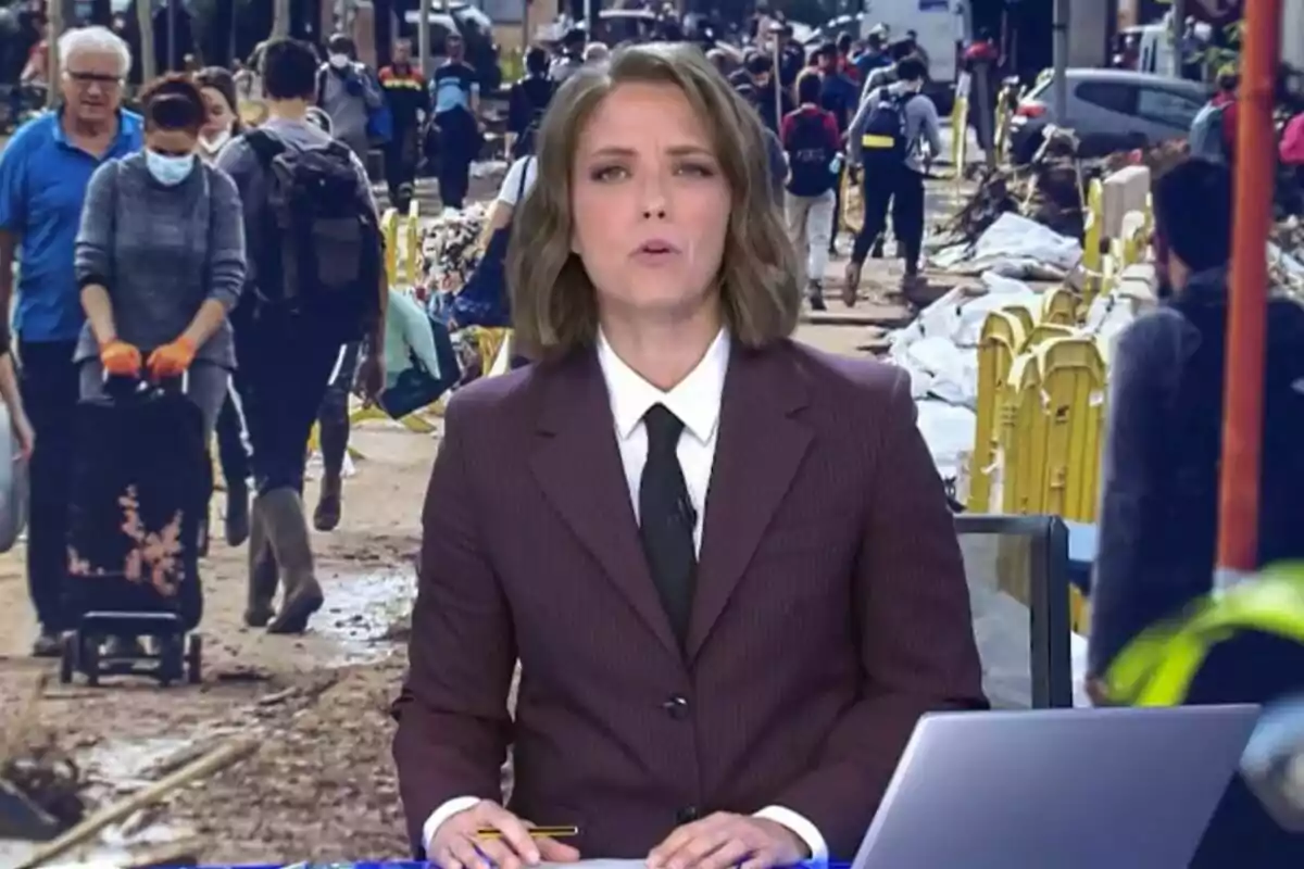 María Casado en Informativos Telecinco en un estudio con una imagen de fondo que muestra a personas caminando por una calle concurrida.