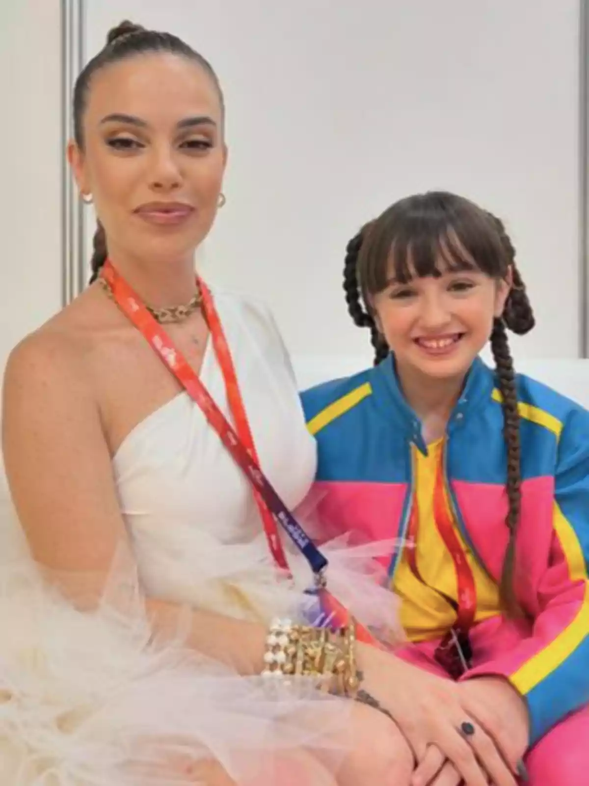 María Isabel y Chloe de la Rosa posan juntas, una mujer con un vestido blanco y una niña con una chaqueta colorida, ambas sonríen y llevan acreditaciones colgadas al cuello. María Isabel y Chloe de la Rosa posan juntas, una mujer con un vestido blanco y una niña con una chaqueta colorida, ambas sonríen y llevan acreditaciones colgadas al cuello.