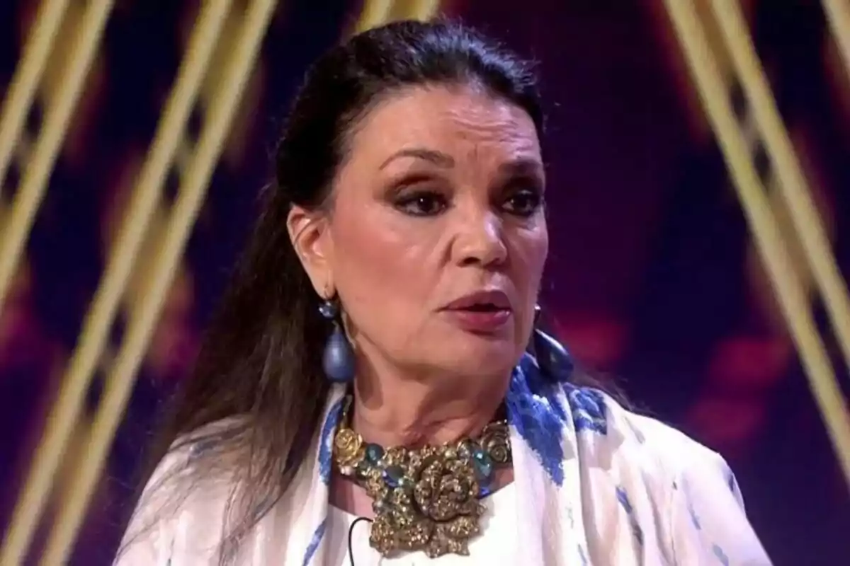 María José Cantudo con cabello oscuro y suelto, usando un collar grande y aretes, está en un escenario con luces de fondo en De Viernes. María José Cantudo con cabello oscuro y suelto, usando un collar grande y aretes, está en un escenario con luces de fondo en De Viernes.