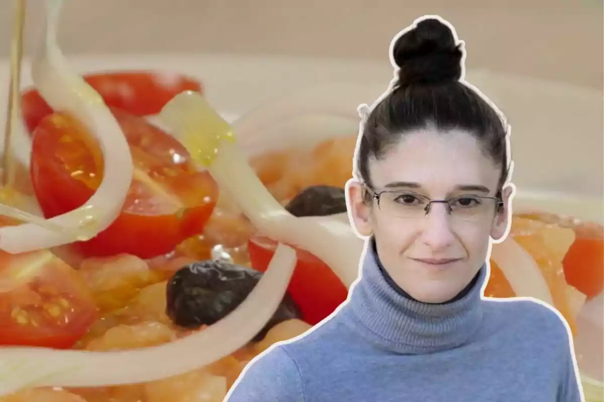 Una mujer con gafas y cabello recogido frente a un plato de ensalada con tomates cherry, cebolla y aceitunas.