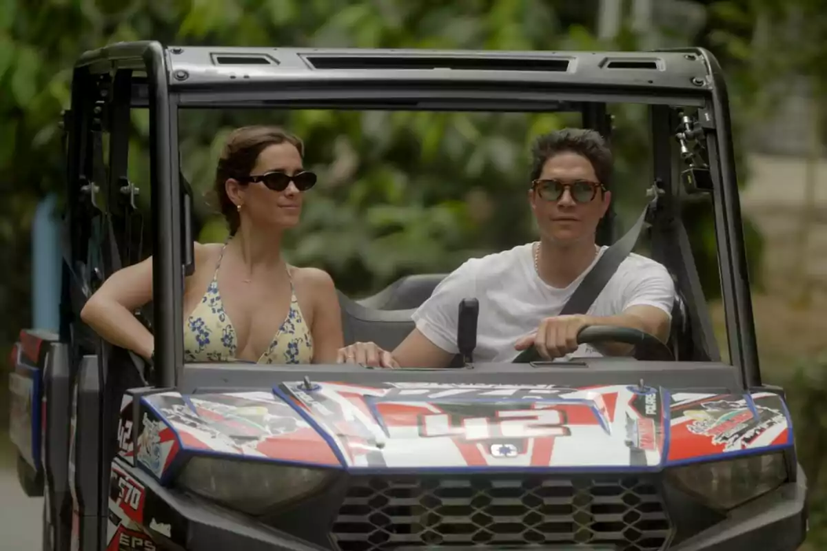 Fotografía de María Pombo y Pablo Castellano con gafas de sol conduciendo un vehículo todoterreno decorado con calcomanías coloridas en su serie en Prime Video