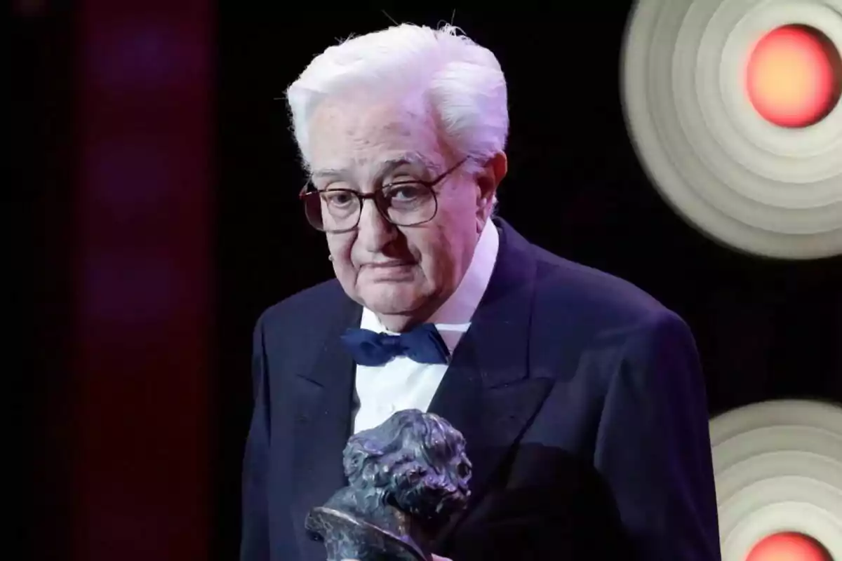 Mariano Ozores mayor con gafas y cabello blanco sostiene un trofeo en un evento formal. Mariano Ozores mayor con gafas y cabello blanco sostiene un trofeo en un evento formal.