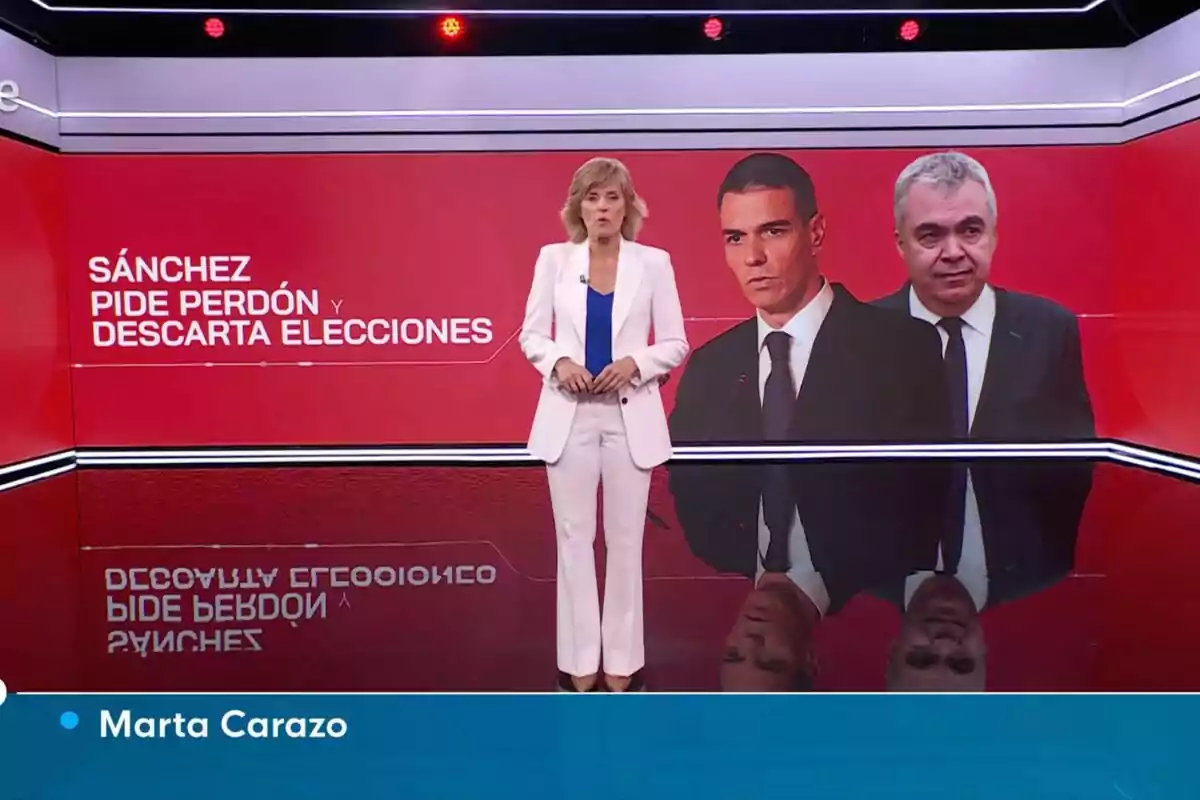 Presentadora de informativos de pie, Marta Carazo, en un estudio de televisión con fondo rojo y dos hombres en pantalla junto al texto Sánchez pide perdón y descarta elecciones Presentadora de informativos de pie, Marta Carazo, en un estudio de televisión con fondo rojo y dos hombres en pantalla junto al texto Sánchez pide perdón y descarta elecciones