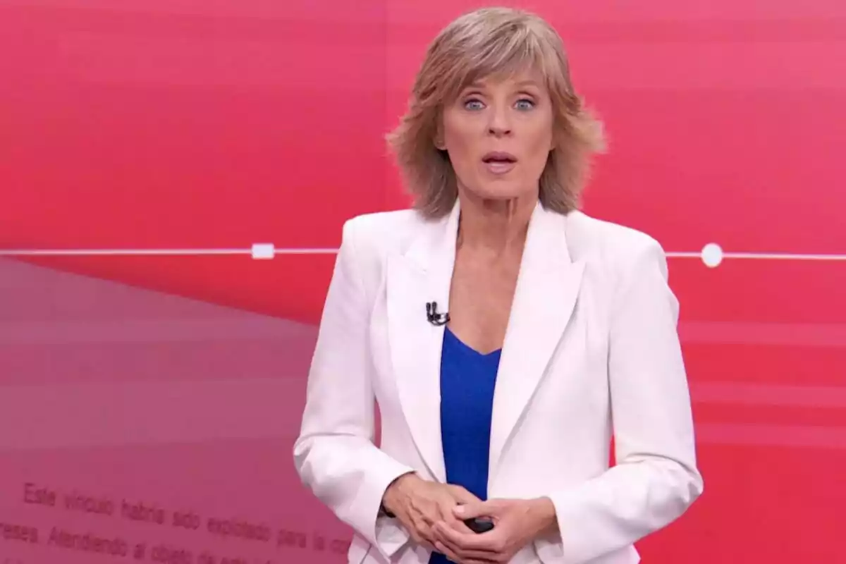 Marta Carazo rubia con saco blanco y blusa azul presentando en un estudio con fondo rojo