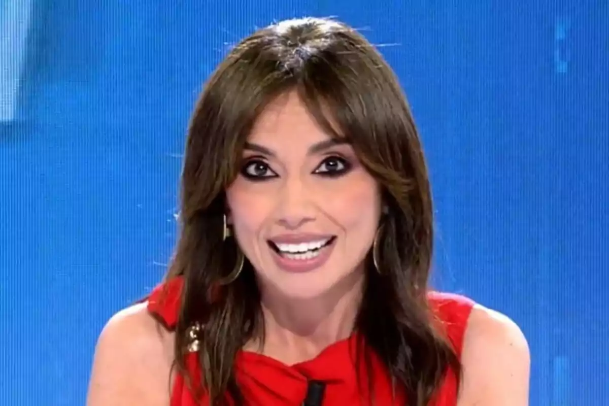 Marta Flich de cabello castaño sonriente con vestido rojo en Todo es Mentira frente a un fondo azul