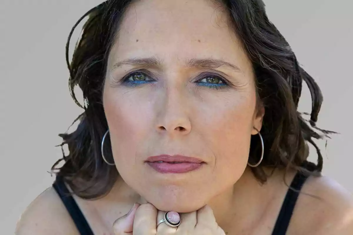 Mujer de cabello castaño y ojos claros mirando de frente con expresión seria y la barbilla apoyada en sus manos Mujer de cabello castaño y ojos claros mirando de frente con expresión seria y la barbilla apoyada en sus manos