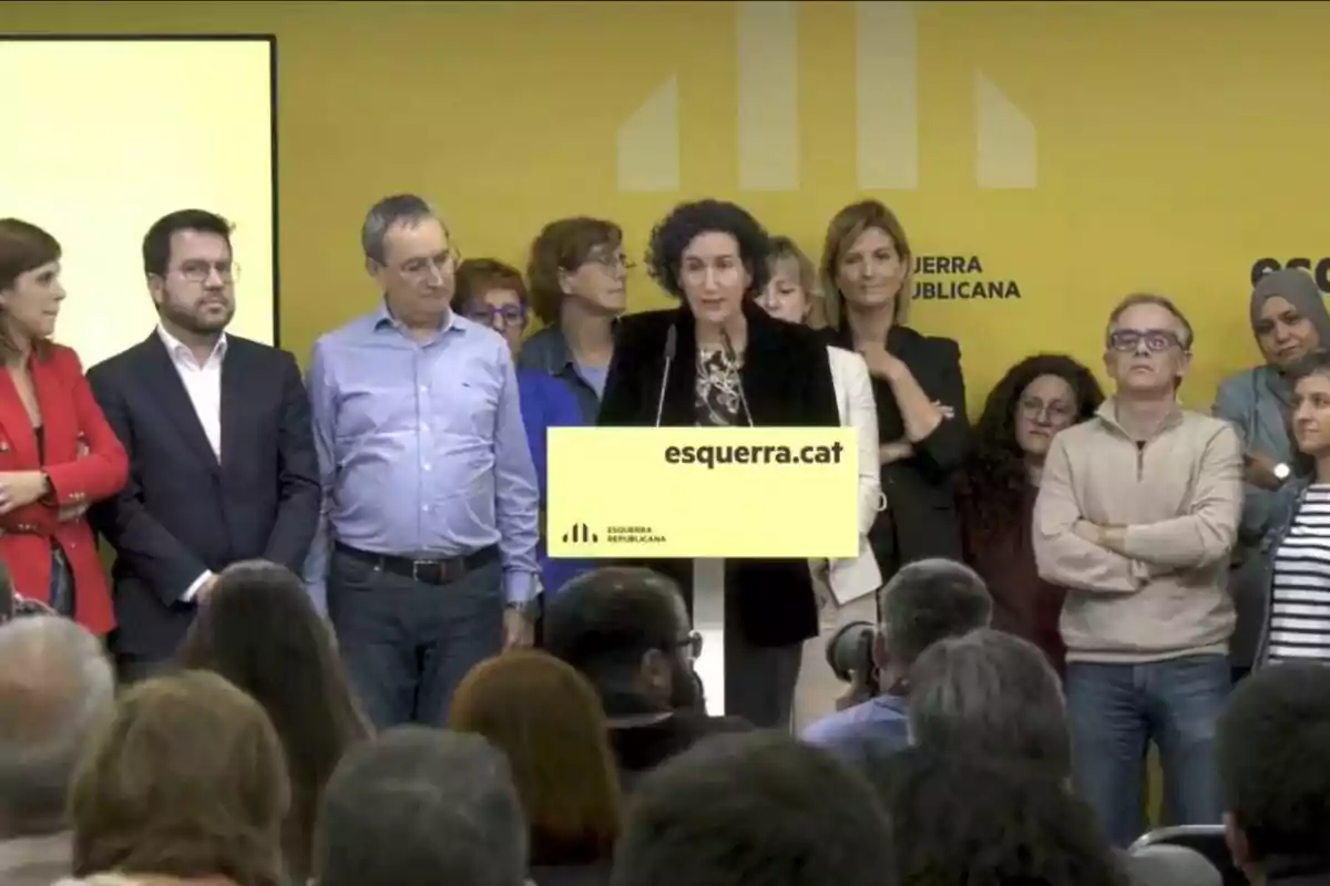 Un grupo de personas en un evento de Esquerra Republicana con una mujer hablando en un podio amarillo frente a una audiencia.